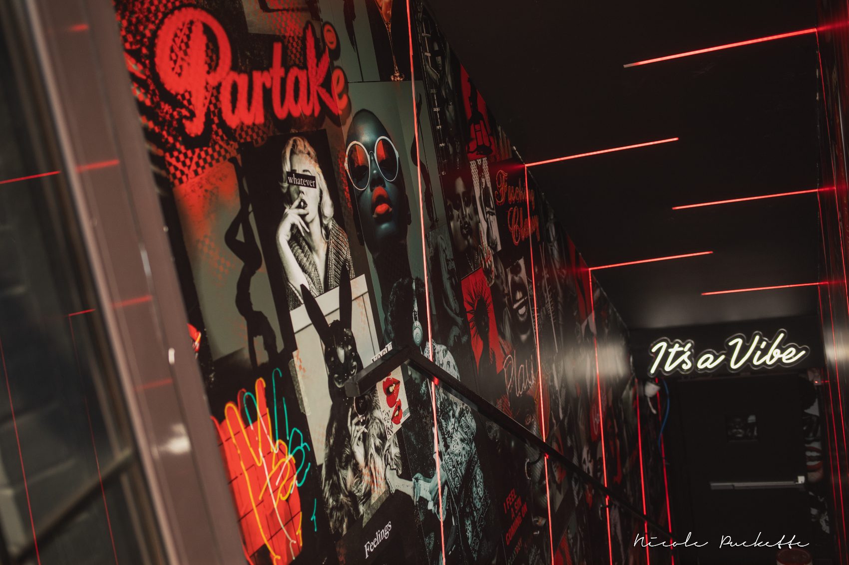Poster-covered stairwell lit in red neon leading down to the Red Room at Partake NYC